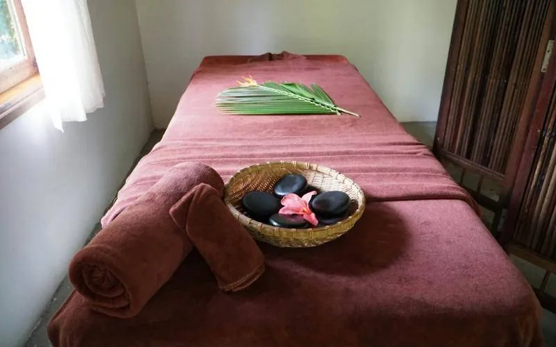 Massage table with rolled towels and a basket of stones